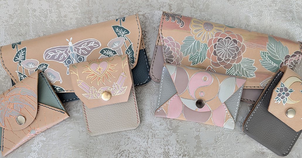 A flat-lay collection of Leather & Light envelope wallets and cardholders with foiled butterfly, crystal, yin-yang and floral designs